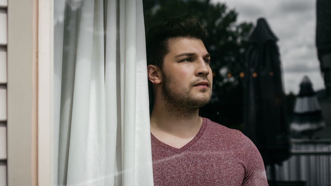 Concerned homeowner looks out the window of their house, symbolizing the anxiety of a home sitting on the market.