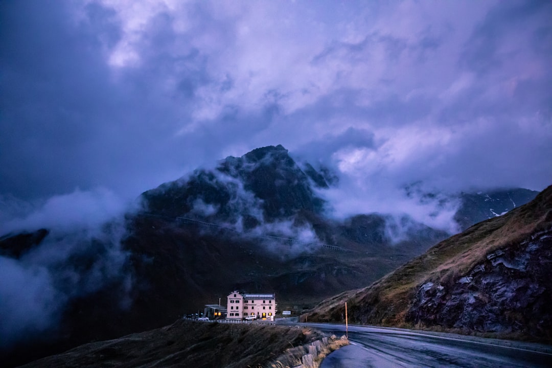 Sturdy house nestled in a hilly, wooded landscape with dramatic storm clouds gathering overhead, symbolizing the need to p...