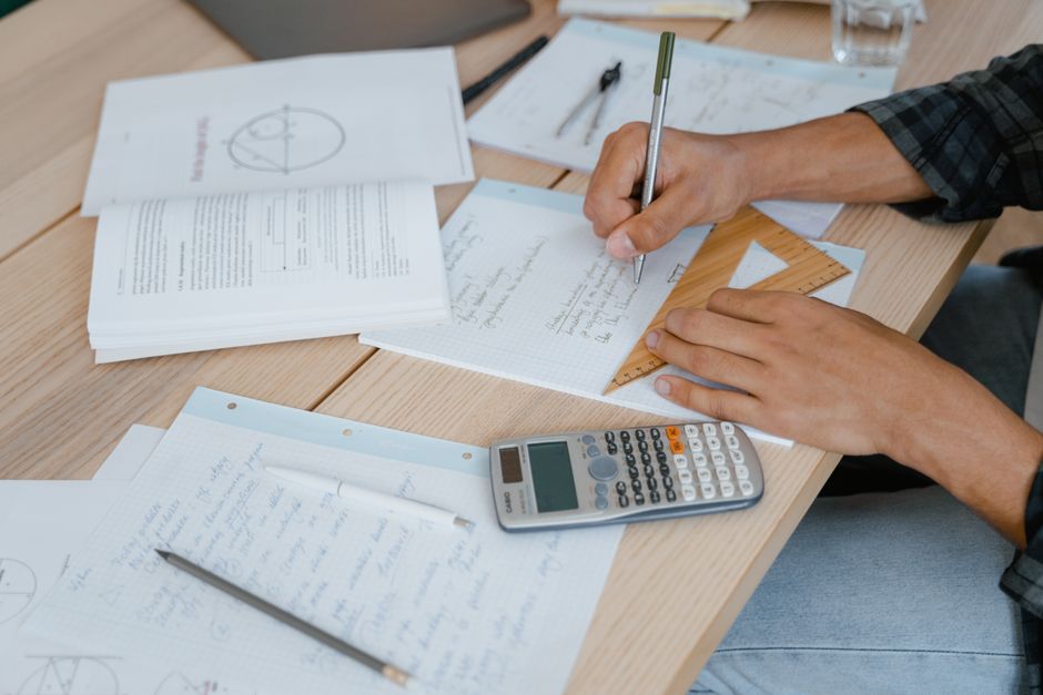 A person's hands are shown calculating finances on a desk next to a small architectural model of a house, illustrating the concept of home equity planning.